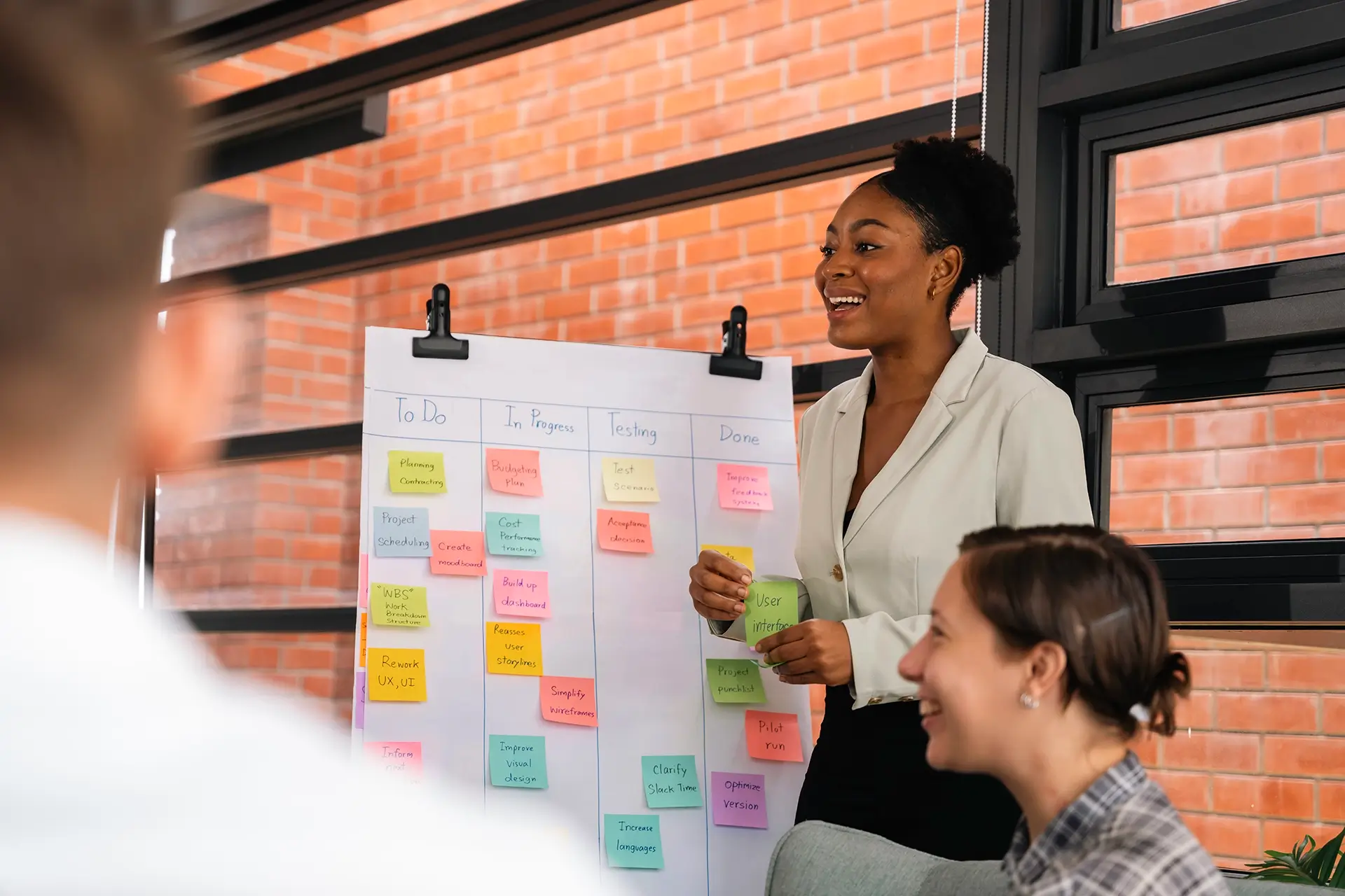 A young woman presenting a project board to a small group.