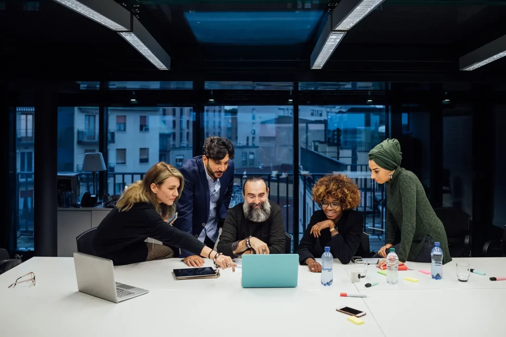 A group of five people collaborating on a project and discussing something on the laptop screen.