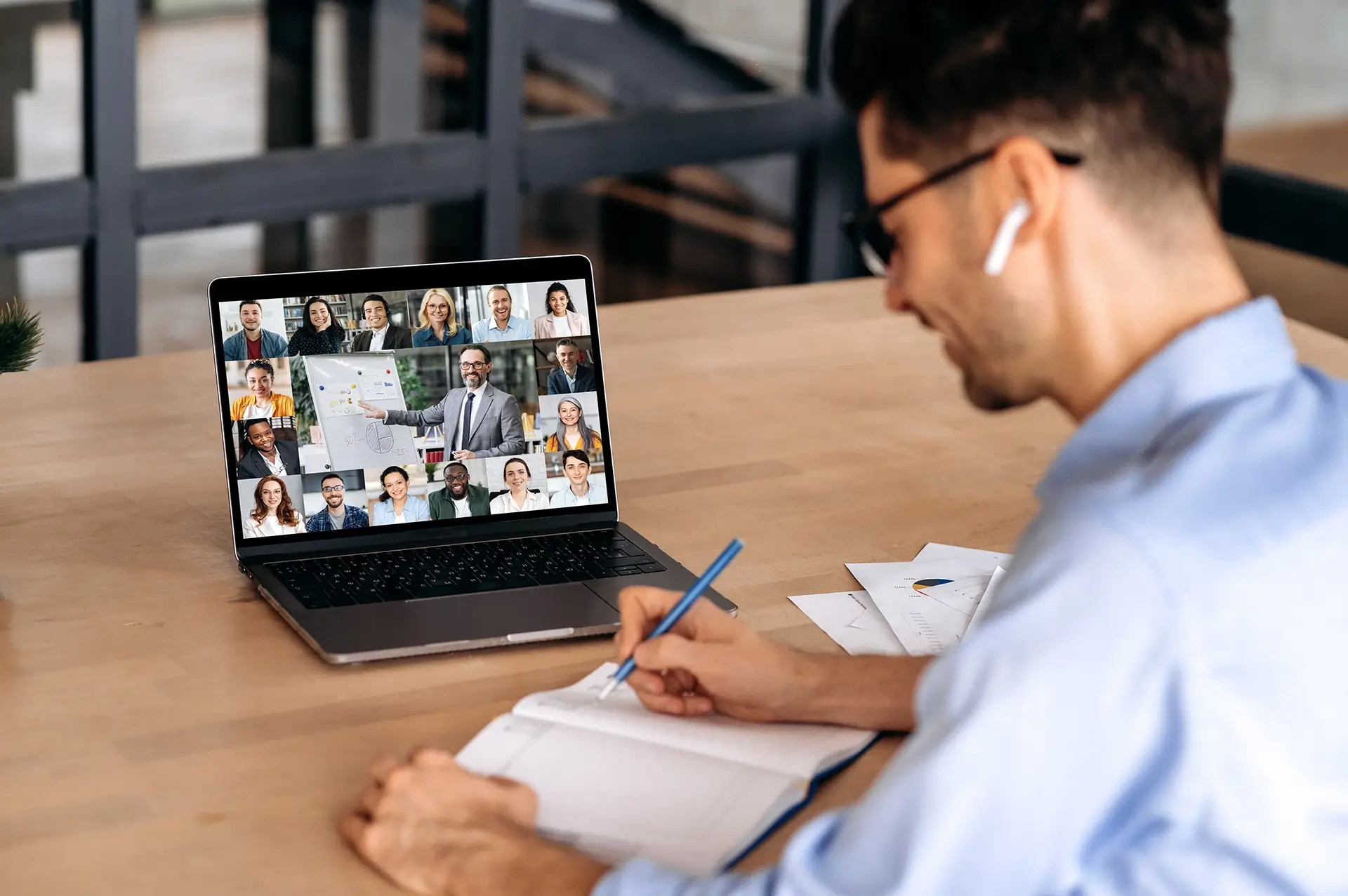 A male office employee, takes notes during online video conference with mature successful ceo and multiracial colleagues, using laptop, sitting in office, planning marketing strategy