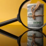 A bundle of money tied with a string viewed through a magnifying glass, symbolizing scrutiny of JPM Coin's dual yield claims.