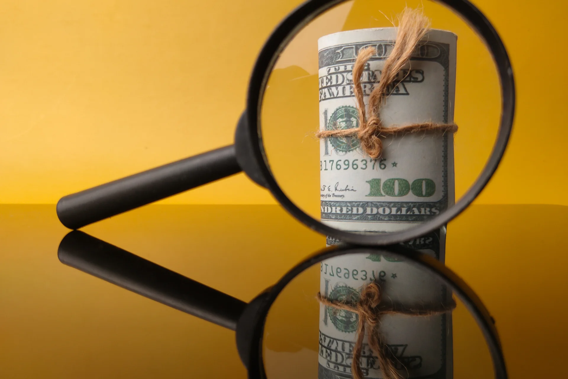 A bundle of money tied with a string viewed through a magnifying glass, symbolizing scrutiny of JPM Coin's dual yield claims.